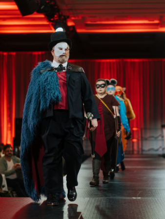 A man walks up the runway with a Phantom of the Opera-type mask and formal wear complete with a cane. This line was designed by a student.