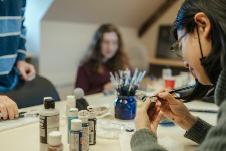 A NBCCD student paints their 3D-printed figure in a classroom. Paintbrushes are on the desk in front of them.