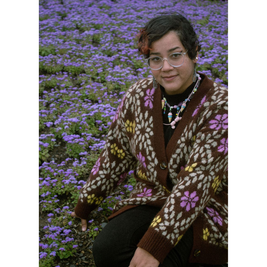 A portrait of Shayra Feliz, an NBCCD tour ambassador. She is in a field of purple flowers with a flower cardigan on.