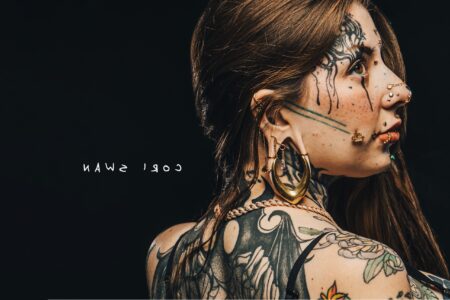 Tattooed woman with piercings photographed in studio light with black background.
