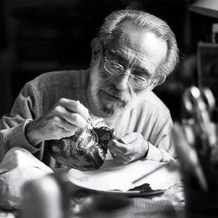 A man wearing glasses works carefully on a 3D work of art.